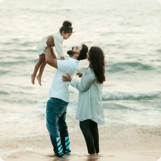 Eltern halten ihr Kind lächelnd hoch in die Luft am Strand.