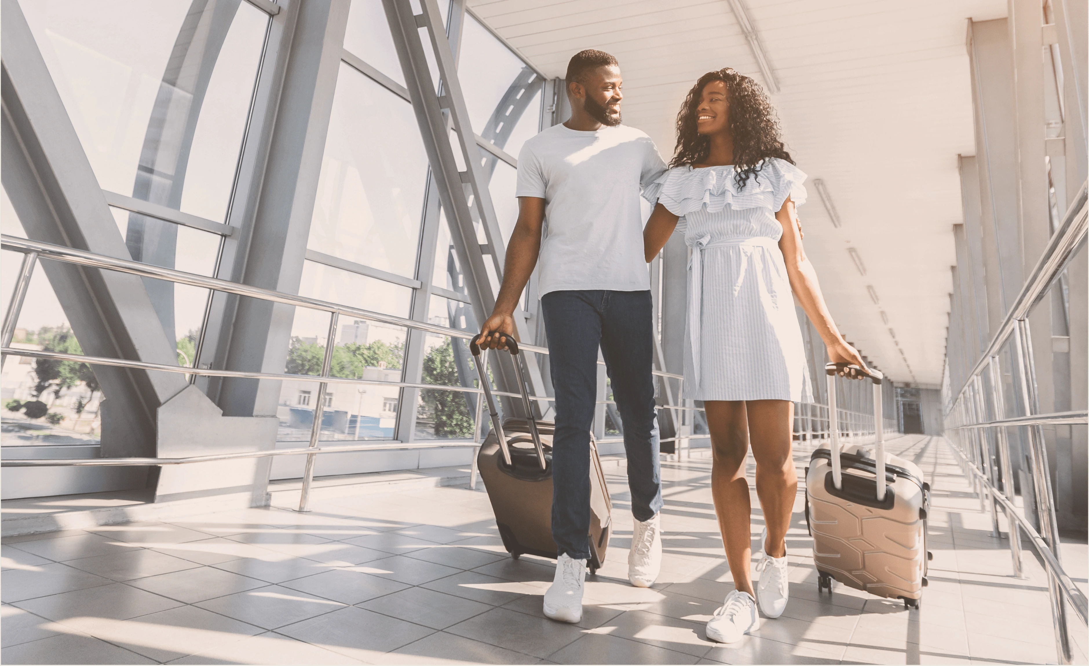 Pärchen läuft lächelnd Arm in Arm am Flughafen und ziehe Koffer hinter sich her.