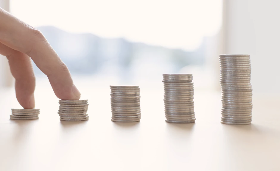 Auf dem Bild sieht man 5 Häufchen mit Geldstücken und eine Hand, die das Geld berührt.