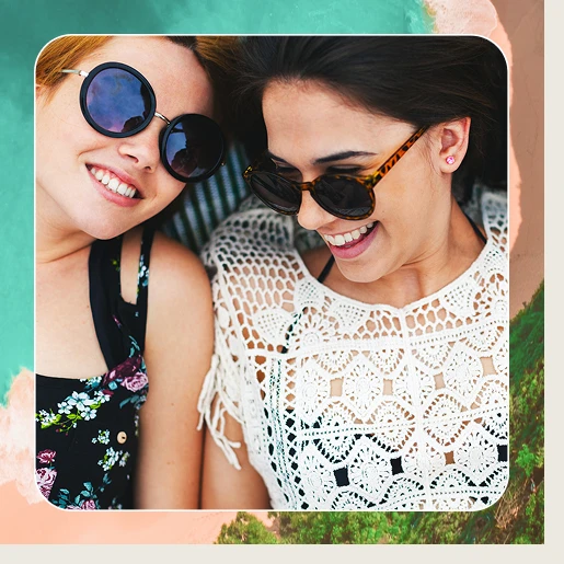 2 Frauen mit Sonnenbrille liegen lachend auf dem Boden. Im Hintergrund ist ein Strandbild von oben abgebildet. Geschrieben steht: "Freunde werben und 500 € Reisegutschein gewinnen.".