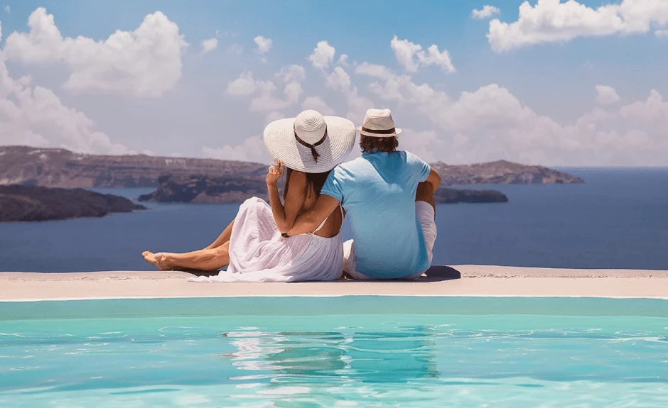 Paar sitzt mit Rücken zur Kamera am Pool und schaut auf eine Bucht.