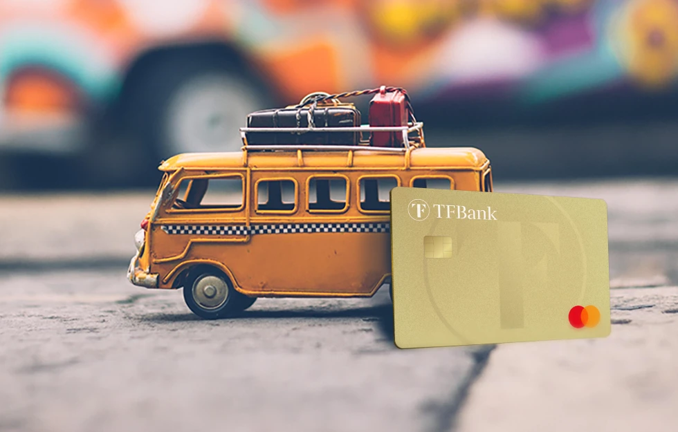 Die TF Mastercard Gold lehnt an einem Modell Van mit Koffern drauf.