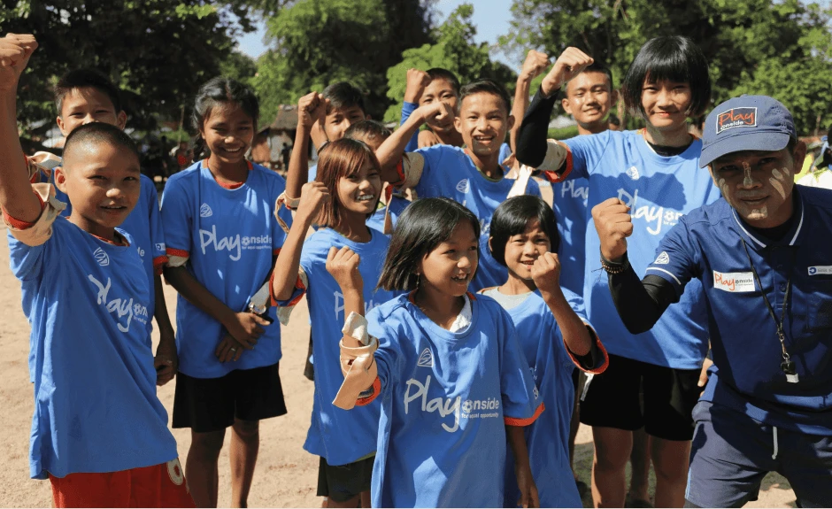 Ein junges Fußball Team steht lächelnd zusammen in einer Gruppe. Einige halten stolz ihre Fäuste nach oben.