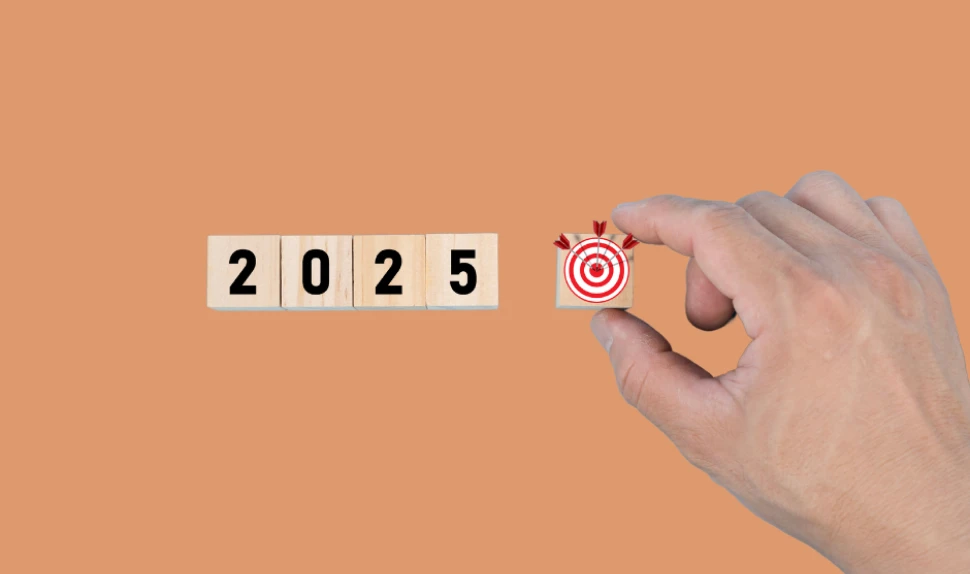 Holzsteine bilden zusammen 2025 auf orangem Hintergrund. Daneben wir eine Zielscheib von einer Hand gehalten.