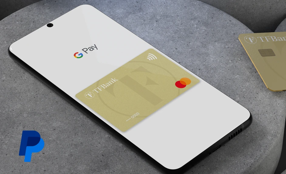 Handy liegt mit geöffnetem Bildschirm auf einer grauen Ablage. Es ist Google Pay mit der TF Mastercard Gold zu sehen. Links unten ist das PayPal Logo abgebildet.