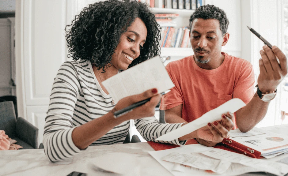 Ein Mann und eine Frau sitzen an einem Tisch in einer Wohnung und schauen sich Dokumente an.