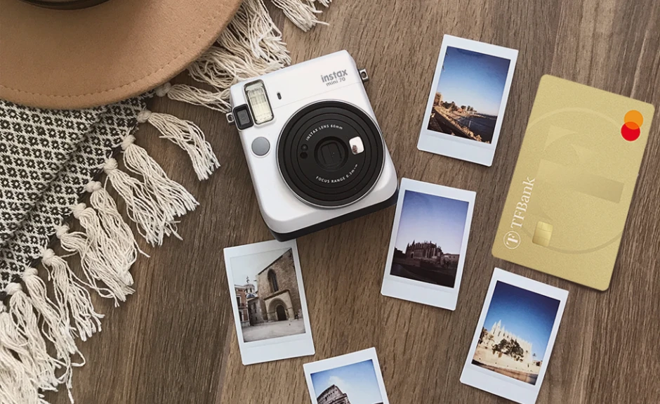 Auf einem Boden liegen Urlaubs-Polaroidbilder, eine Polaroid Kamera, ein Strohhut und die TF Mastercard Gold.