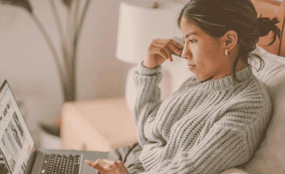 Frau sitzt auf Couch und schaut konzentriert auf Laptop beim Online Shopping.
