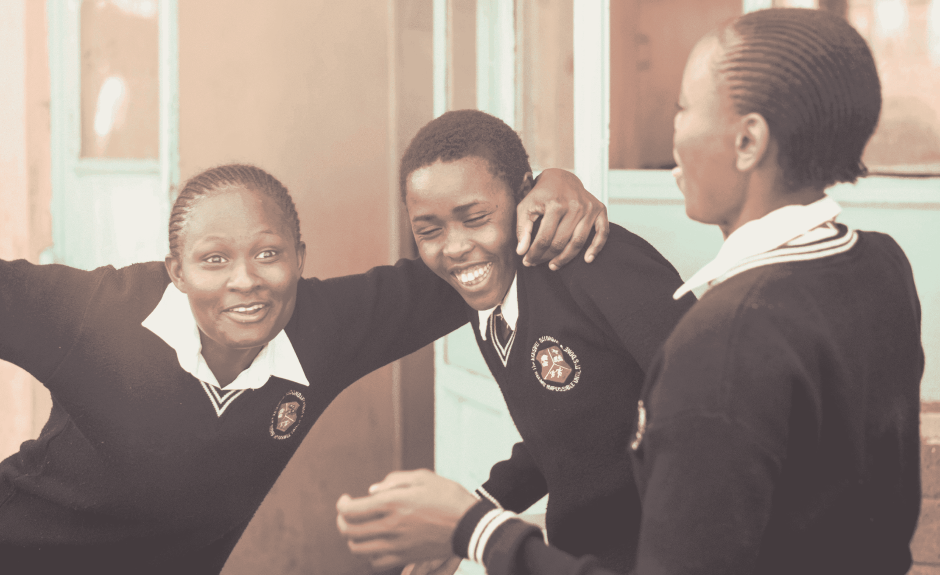 Es sind drei afrikanische Schüler zu sehen. Sie lachen und eine Person stützt sich auf den Schultern einer anderen. 