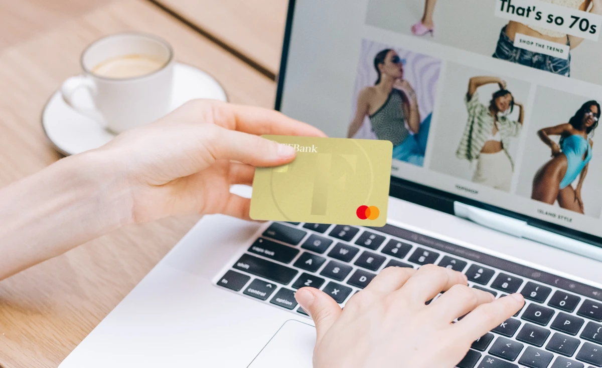 Frau hält Kreditkarte in der Hand, während man auf dem Laptop im Hintegrund einen Online-Shop erkennt