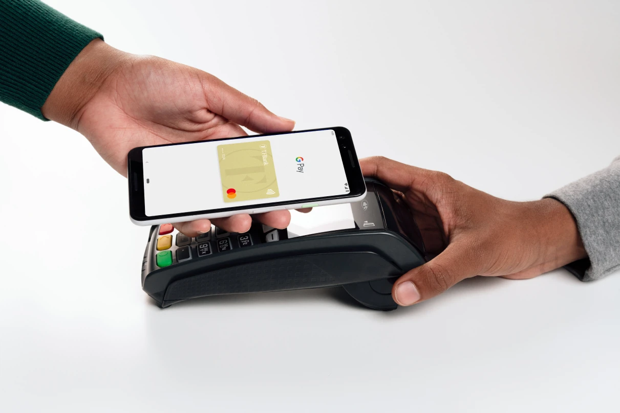 Eine Hand hält ein Handy mit der Google Pay Funktion und integrierter TF Mastercard Gold an ein Kartenlesegerät.