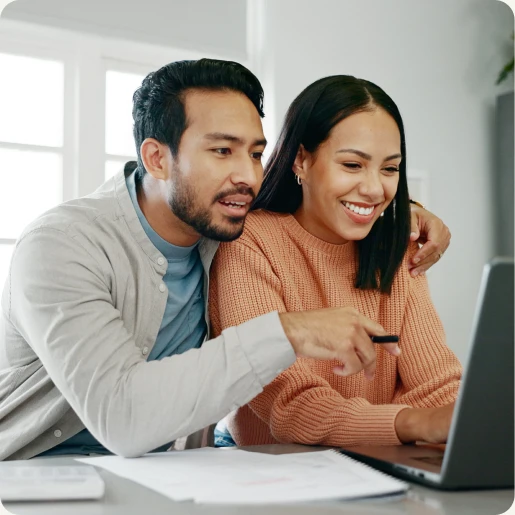 Ein Mann und eine Frau schauen beide auf einen Laptop. Der Mann hat seinen Arm um die Frau gelegt und schaut interessiert. Die Frau lächelt.