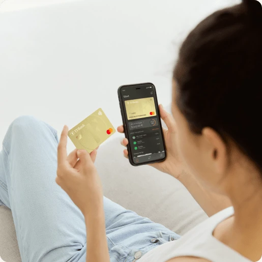 Frau nutzt die TF Bank Mobile App auf ihrem Smartphone. Daneben hält sie die physische TF Mastercard Gold.