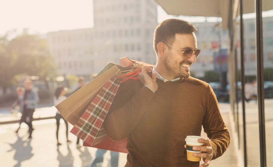 Mann läuft durch die Stadt mit Shoppingtüten und lacht.