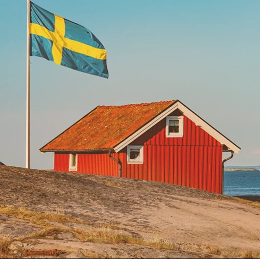 Rotes, schwedisches Haus am Wasser. Neben dem Haus ist eine schwedische Flagge